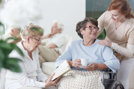 Two elder ladies in glasses spending time together in common room of nursing home