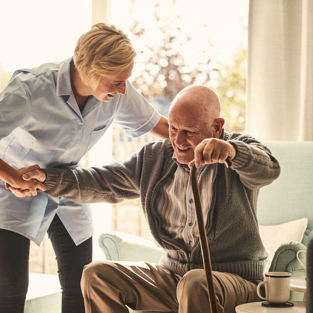 A nurse helping an elderly man out of a chair