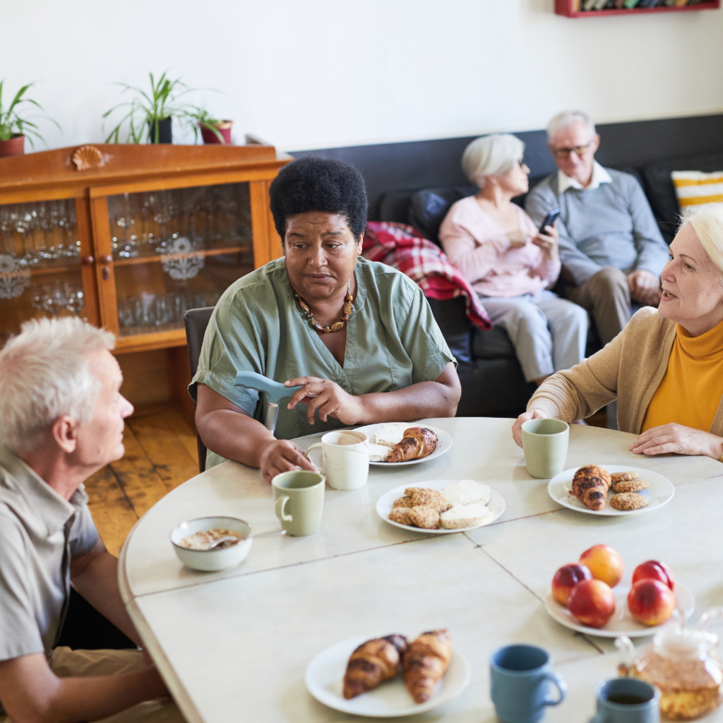 Community living space in a care setting, where 3 people are having a conversation over breakfast.