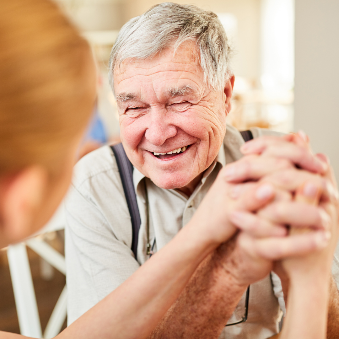 An elderly man clutching hands with a nurse, smiling